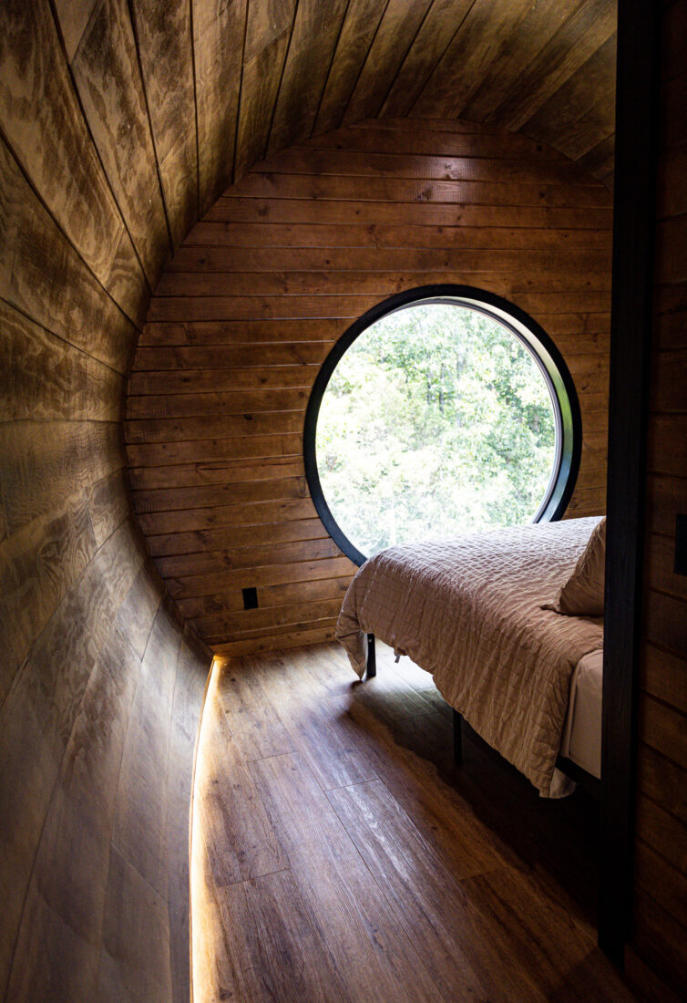 Inside a circular wooden room with a circular window and a bed