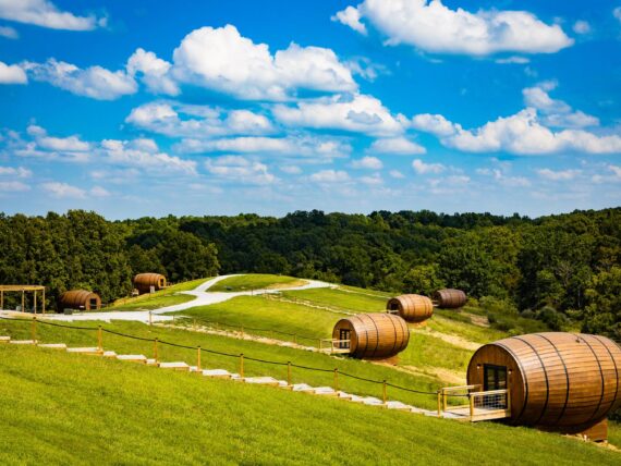 A grassy hill dotted with large bourbon barrel-shaped cabins