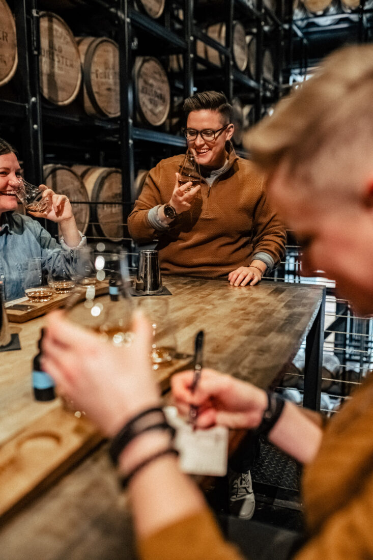 People at a table laugh and drink bourbon and take notes