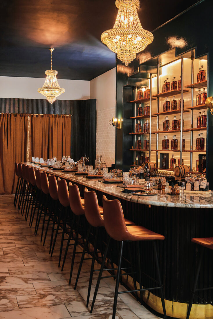 Inside a bar with a long marble bartop and skinny bar chairs with leather seats