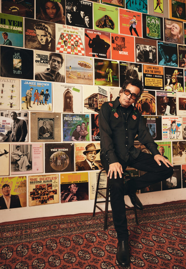 A man sits on a chair by a wall of records