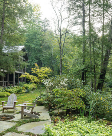 A garden at the back of a house in woodland. It has a firepit surrounded by chairs
