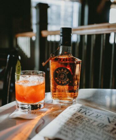 A red cocktail by a bottle of bourbon