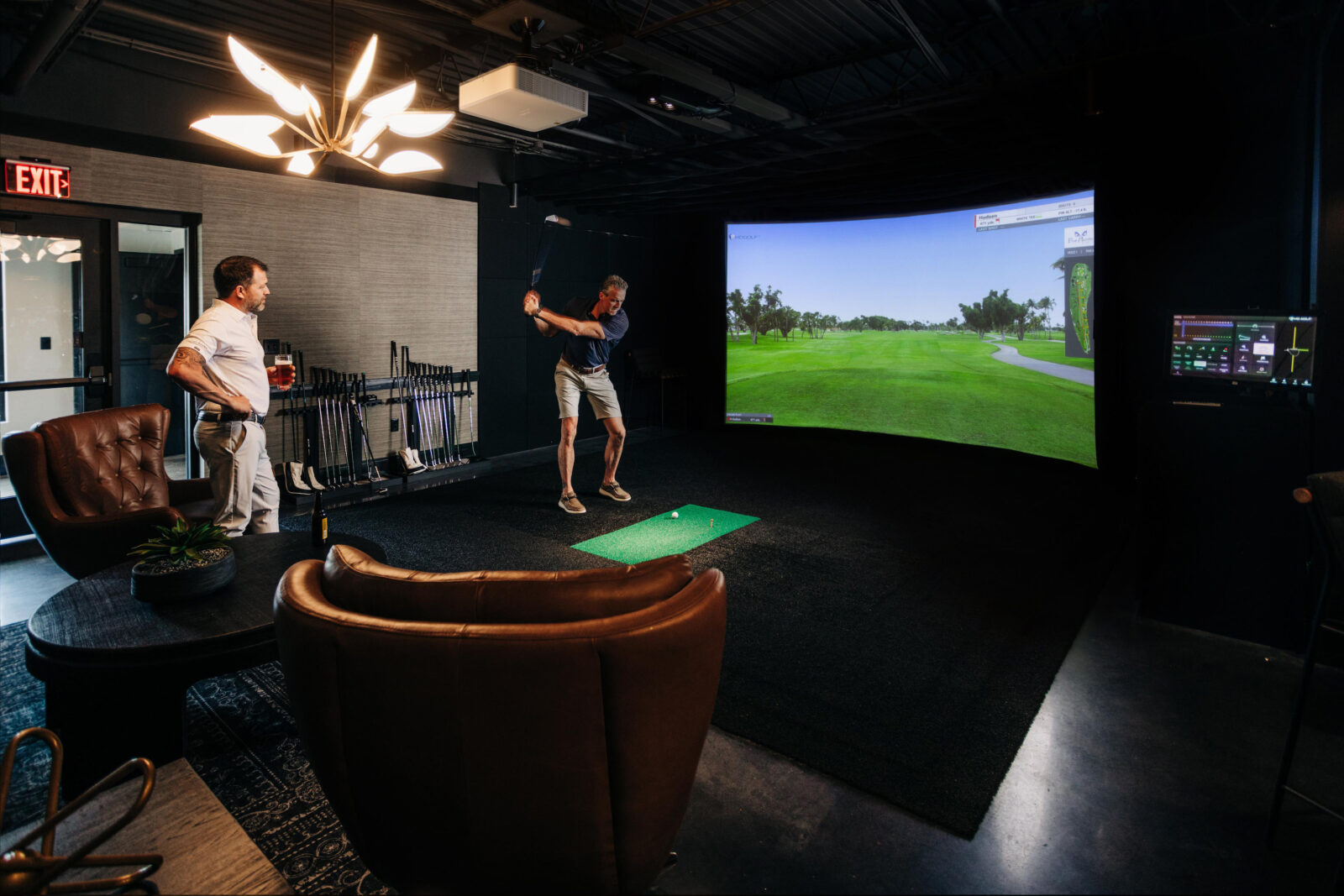 Two men practice golf swings on a simulator