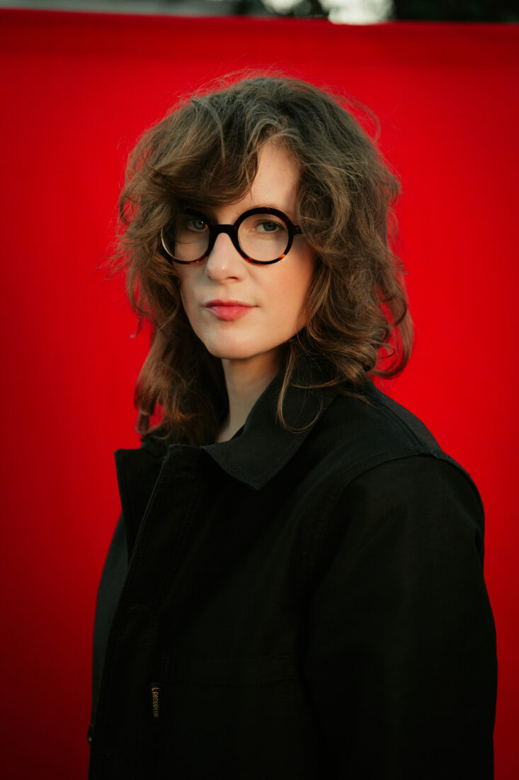 A portrait of a woman with glasses in front of a red background