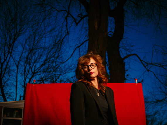 A woman with glasses stands outside in front of a red drop cloth